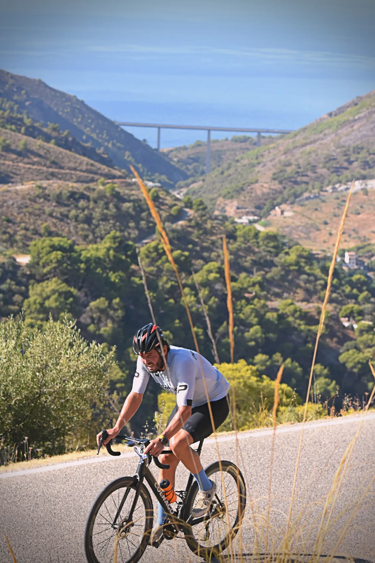 Ciclista de BYB Training subiendo Los Castillejos con el mar al fondo — entrenador de ciclismo online en la Axarquía, Málaga