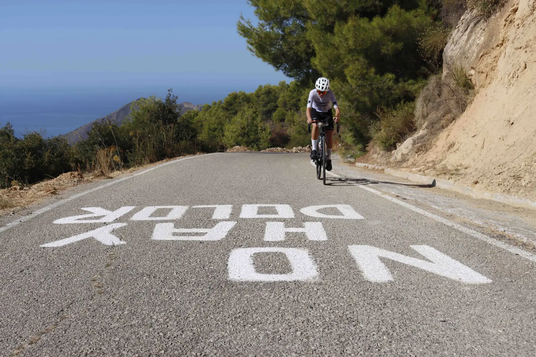 Ciclista de BYB Training subiendo a Los Castillejos sobre la pintada «No hay dolor»